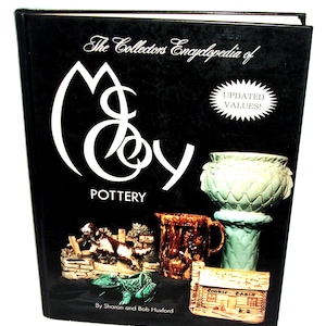 以下が含まれることがあります： 「The Collectors Encyclopedia of McCoy Pottery」と題された黒い本で、表紙には「UPDATED VALUES！」と書かれています。表紙には、茶色、緑、タン色の様々なマッコイ陶器の画像が掲載されています。