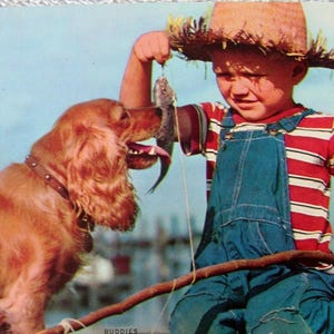 Puede incluir: Imagen de postal vintage de un niño con peto vaquero y sombrero de paja, pescando. El niño sostiene un pez pequeño, mientras que un perro marrón con collar lo alcanza. El niño lleva una camisa a rayas rojas y blancas. El fondo es azul.