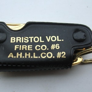 May include: A black leather keychain with a gold metal key ring. The keychain has the text "BRISTOL VOL. FIRE CO. #6 A.H.H.L.CO. #2" engraved in gold.