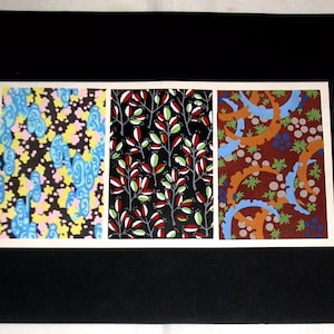 Puede incluir: Tres patrones de tela diferentes se muestran sobre un fondo negro. El primer patrón es un fondo negro con remolinos azules, amarillos y rosados. El segundo patrón es un fondo negro con hojas rojas y verdes. El tercer patrón es un fondo marrón con remolinos azules y naranjas.