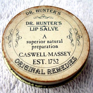 May include: A round metal tin of Dr. Hunter's Lip Salve by Caswell-Massey. The cream-colored lid features black text reading Dr. Hunter's Lip Salve, A superior natural preparation, Caswell-Massey, Est. 1752, and Original Remedies with decorative flourishes.