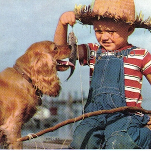 Puede incluir: Un niño pequeño con un sombrero de paja y un mono sostiene un pez mientras un cocker spaniel marrón dorado observa.