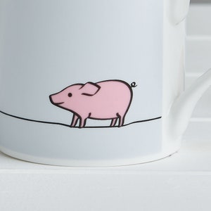 May include: A white ceramic mug with a light blue background and a black line drawing of a pink pig. The pig is walking to the right and has a curled tail.