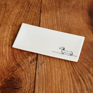 Puede incluir: Un plato rectangular de cerámica blanca con una ilustración en blanco y negro de un perro salchicha.