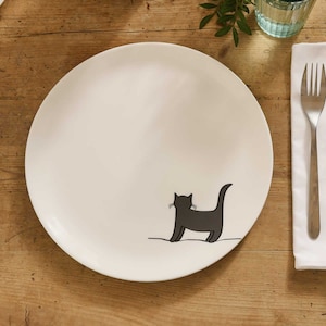 May include: A white ceramic dinner plate featuring a black silhouette of a cat looking to the right. The cat is facing away from the viewer.