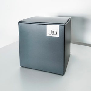 May include: A dark gray square box with a white label that says "Jin Designs".