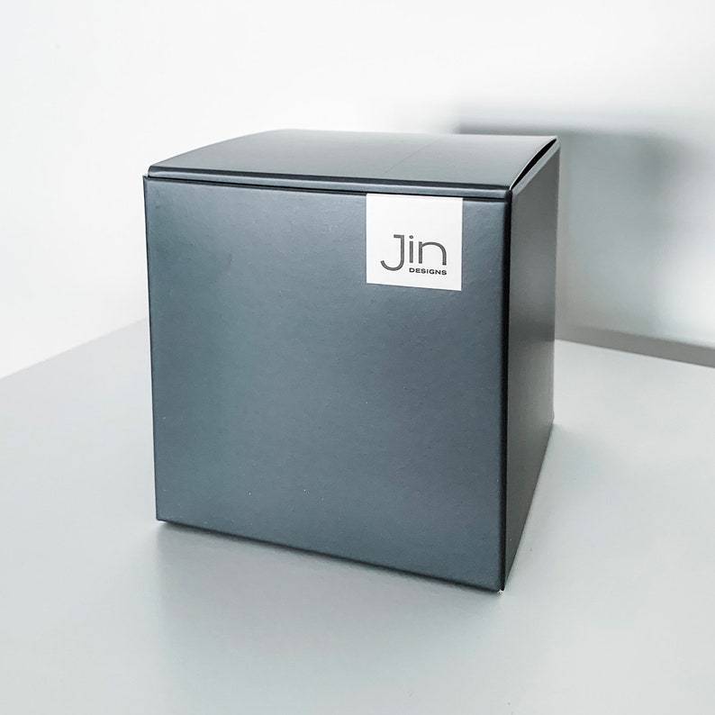 May include: A dark gray square box with a white label that says "Jin Designs".