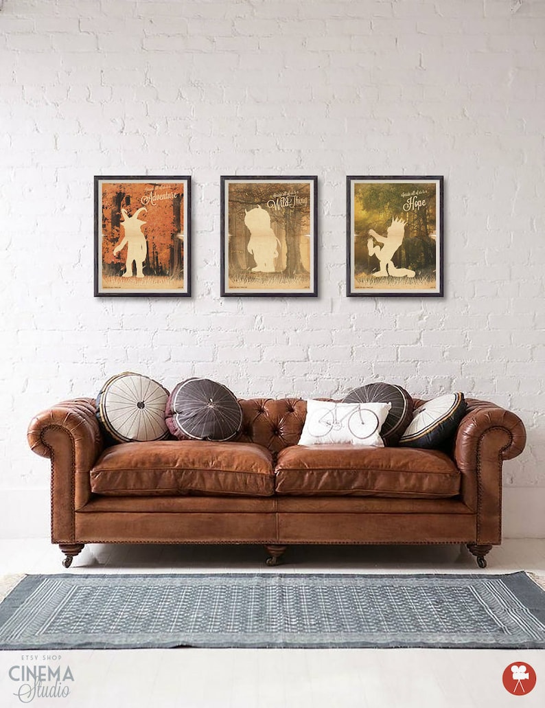 May include: Three framed prints with a white silhouette of a creature from the book Where the Wild Things Are. The prints are hung on a white brick wall above a brown leather sofa with pillows. The prints are titled "Adventure", "Wild Thing", and "Hope".