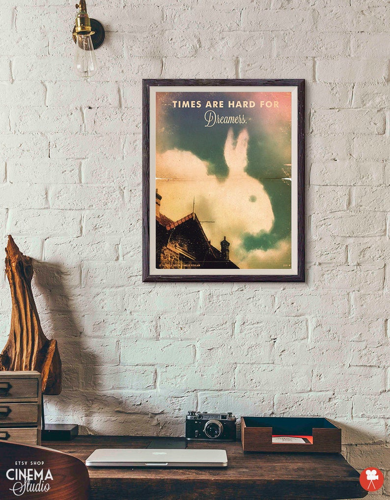 Puede incluir: Un p&oacute;ster de estilo vintage con un fondo descolorido y texturado que presenta una nube de conejo blanco sobre un edificio. El texto en el p&oacute;ster dice "Times are hard for Dreamers."