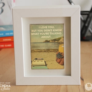 May include: A white framed print with a vintage aesthetic featuring a beach scene with a record player and a quote that reads "I love you, but you don't know what you're talking about."