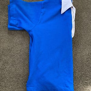 May include: A blue short-sleeved shirt with a white collar. The shirt is folded and laid flat on a brown surface.