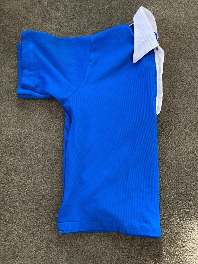 May include: A blue short-sleeved shirt with a white collar. The shirt is folded and laid flat on a brown surface.