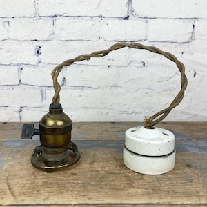 May include: A vintage brass light socket with a porcelain ceiling fixture and a brown cloth-covered wire.