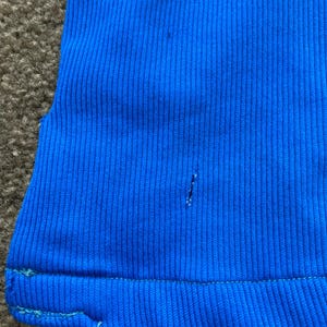 May include: A close-up of a bright blue ribbed fabric with a small hole in the centre. The fabric has a subtle sheen and a slightly textured surface.