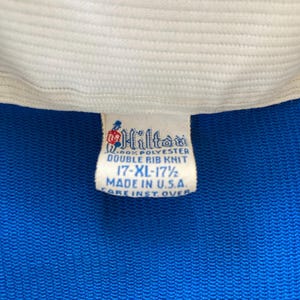 May include: A white tag with blue text that reads "Hilton 100% Polyester Double Rib Knit 17-XL-17 1/2 Made in U.S.A. Care Inst. Over"