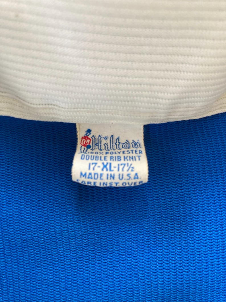 May include: A white tag with blue text that reads "Hilton 100% Polyester Double Rib Knit 17-XL-17 1/2 Made in U.S.A. Care Inst. Over"