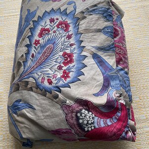 Puede incluir: Ropa de cama doblada con un estampado floral en tonos azules, rojos y morados sobre un fondo beige. El dise&ntilde;o presenta grandes flores y follaje estilizados.