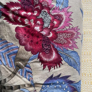 Puede incluir: Primer plano de una tela con un gran estampado floral. El dise&ntilde;o presenta una gran flor estilizada en tonos magenta, rosa y blanco, con acentos azules y marrones sobre un fondo neutro. La tela tiene un aspecto suave y texturizado.