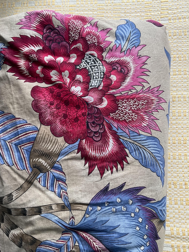 Puede incluir: Primer plano de una tela con un gran estampado floral. El dise&ntilde;o presenta una gran flor estilizada en tonos magenta, rosa y blanco, con acentos azules y marrones sobre un fondo neutro. La tela tiene un aspecto suave y texturizado.