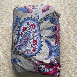 Puede incluir: Tela doblada con un estampado floral en tonos azules, rosas y grises. El dise&ntilde;o presenta grandes flores y hojas estilizadas. La tela est&aacute; doblada cuidadosamente, mostrando el intrincado patr&oacute;n.