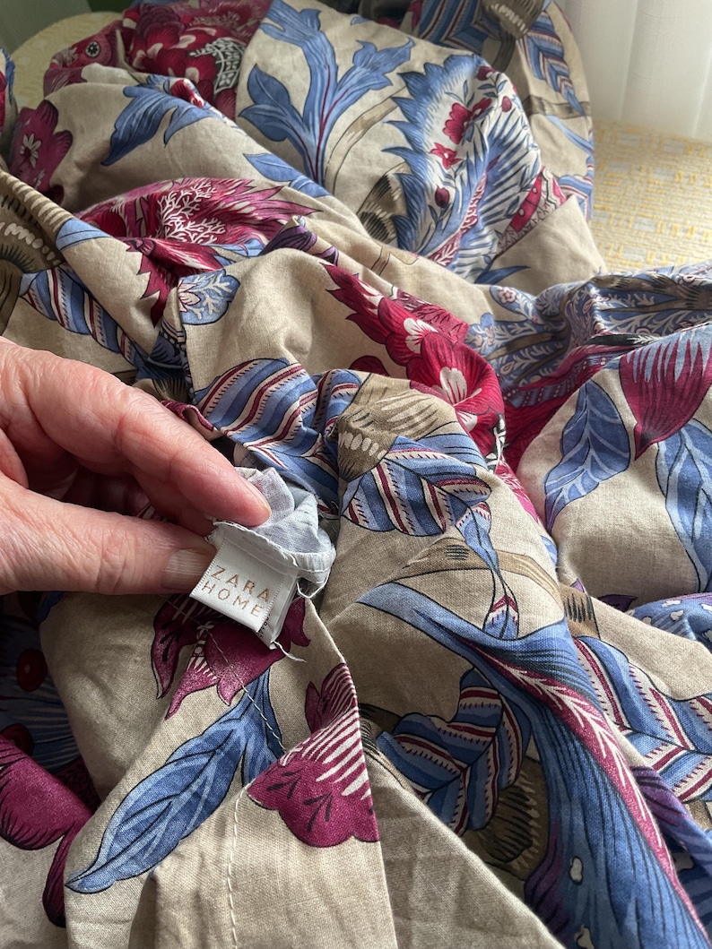 Puede incluir: Tela beige con estampado floral en azul y burdeos. El dise&ntilde;o presenta un estampado bot&aacute;nico a gran escala. La etiqueta dice "ZARA HOME".