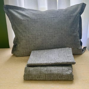 May include: A rectangular pillowcase and two folded fabric pieces featuring a grey and white cross-hatched pattern. The pillowcase has a wide flange border, while the two folded textile items display the same consistent textured linear design.