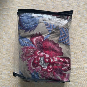 Puede incluir: Un juego de cama empaquetado con un gran estampado floral en tonos borgo&ntilde;a, rosa, azul y gris. El dise&ntilde;o es visible a trav&eacute;s del embalaje de pl&aacute;stico transparente, mostrando los intrincados detalles del estampado bot&aacute;nico.