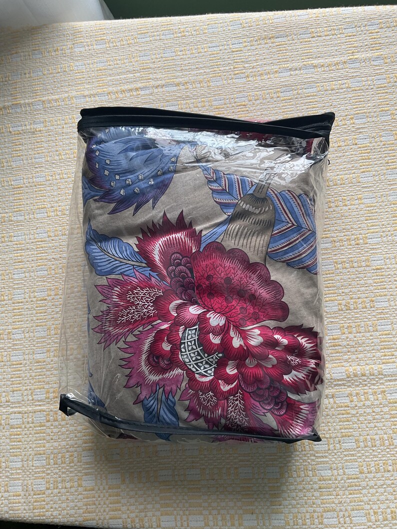 Puede incluir: Un juego de cama empaquetado con un gran estampado floral en tonos borgo&ntilde;a, rosa, azul y gris. El dise&ntilde;o es visible a trav&eacute;s del embalaje de pl&aacute;stico transparente, mostrando los intrincados detalles del estampado bot&aacute;nico.