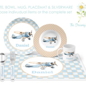 May include: A blue and white airplane themed children's dinnerware set with a plate, bowl, mug, placemat, and silverware. The set features a blue airplane with a brown propeller and the name "Daniel" on each piece.