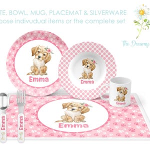 May include: Pink and white personalized children's dinnerware set with a dog illustration. The set includes a plate, bowl, mug, placemat, and silverware. The text "Emma" is printed on each piece.