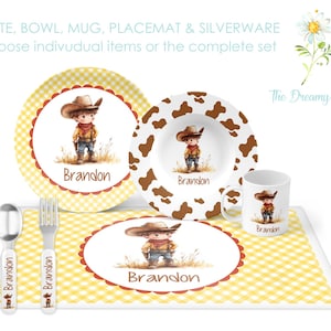 May include: A personalized children's place setting with a cowboy theme. The set includes a yellow and white checkered placemat, a white plate with a yellow and white checkered border, a white bowl with a brown cow print, a white mug with a brown cow print, and two silver utensils. The place setting is decorated with a cartoon cowboy wearing a brown hat and a red bandana. The name "Brandon" is printed on each piece.