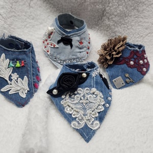 May include: Four denim dog collars with different embellishments. One collar has a white lace floral design, another has a black rose and white lace, another has a burgundy lace with pearls, and the last has a brown fabric flower and rhinestones.