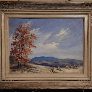 May include: An oil painting in a decorative wooden frame depicting an autumn landscape with a vibrant orange tree in the foreground, a field with small haystacks, and distant blue mountains under a cloudy sky. The artist signature Combe is visible.