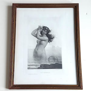 May include: A framed black and white print of a mermaid in the water, holding a seashell. The print is in a brown and gold ornate frame. The text "THE MERMAID" is at the bottom of the print.