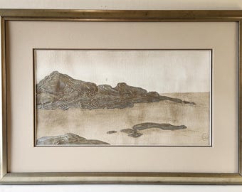 May include: Framed artwork depicting a coastal landscape. The artwork features a textured, raised relief of a rocky shoreline in shades of gray and brown. The artwork is framed in a gold-toned metal frame.
