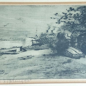 May include: A framed monochrome etching of a coastal landscape. The artwork shows a shoreline with buildings, boats, and trees. The artist's signature and the date 1929 are visible in the lower part of the artwork.