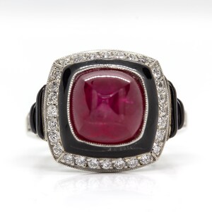 May include: A square-shaped ring with a large red gemstone surrounded by a black enamel border and a halo of small diamonds.