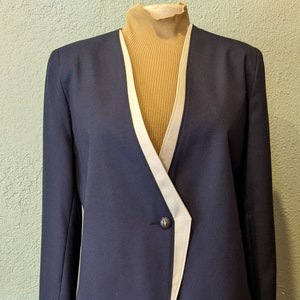 May include: A navy blue skirt suit with a white trim on the jacket. The jacket has a single button closure and a v-neck.