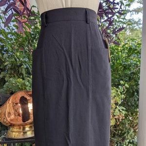 Könnte beinhalten: Ein schwarzer Midirock mit einem Schlitz vorne und einer hohen Taille. Der Rock ist aus einem glatten, knitterarmen Stoff.
