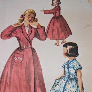 May include: Vintage sewing pattern for a girl's robe and slippers. The pattern includes instructions for two different styles, one with a pink robe and the other with a blue and white floral robe. The pattern also includes a transfer sheet with over 120 different names.
