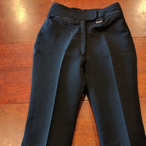 May include: Black tailored trousers with a straight leg and a zip detail on the front. The trousers have belt loops and a small metal tag on the right side of the waistband.