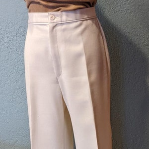 Puede incluir: Pantalón blanco de pierna ancha con una blusa sin mangas de color marrón de punto de canalé y una bufanda estampada. El pantalón tiene cierre de botón y una raya central.