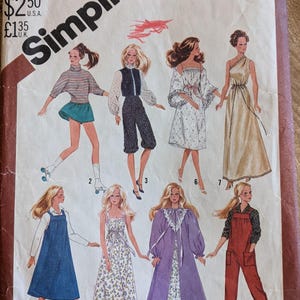 May include: Vintage Simplicity sewing pattern envelope featuring illustrations of various women's clothing designs. The designs include dresses, jumpsuits, and a robe. The envelope is aged with visible wear and tear, and the text "Simplicity" is prominently displayed.