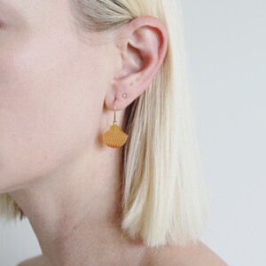 May include: A pair of gold earrings with a fan-shaped shell design in a warm amber colour.