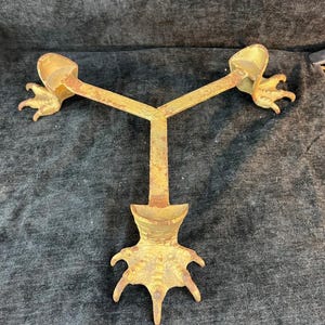May include: A vintage, golden-toned metal object with a Y-shaped design. At each end of the Y are claw-like feet, and at the base is a similar foot design. The object appears to be an antique decorative piece.