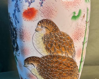May include: A white ceramic vase with a gold rim, featuring hand-painted birds and floral designs in shades of brown, orange, red, purple, and green. The vase has a bulbous shape and a narrow neck.