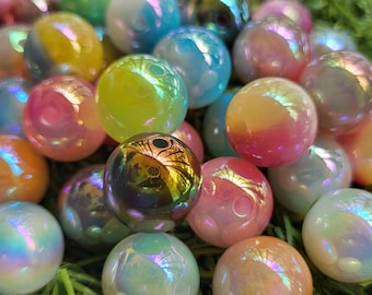 May include: A collection of iridescent glass marbles in various colors, including pink, yellow, blue, and green. The marbles have a glossy, reflective surface and are scattered on a bed of green grass.