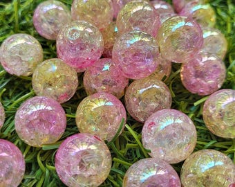 May include: A collection of iridescent, spherical decorative objects in shades of pink, yellow, and clear. The spheres are clustered together on a bed of green artificial grass, creating a visually appealing display.