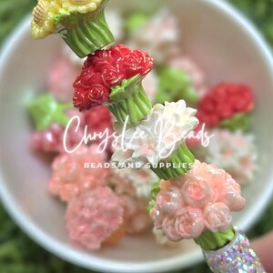 May include: A pen featuring a stack of floral beads in yellow, red, white, and light pink, each with green stems. The base of the pen is covered in iridescent crystals. The text Chrystee Beads BEADS AND SUPPLIES is visible in the center.