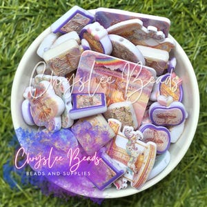 May include: A collection of assorted acrylic beads in a white bowl, featuring various shapes including squares, rectangles, and carousel-themed designs. The beads display a color palette of purple, pink, and gold with printed imagery of merry-go-rounds.